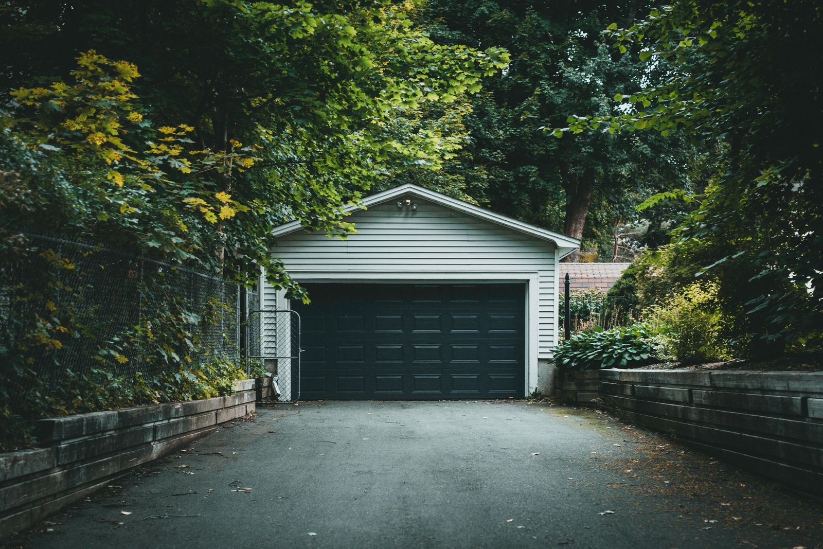 Detached garage with a dark overhead door at the end of a tree-lined driveway