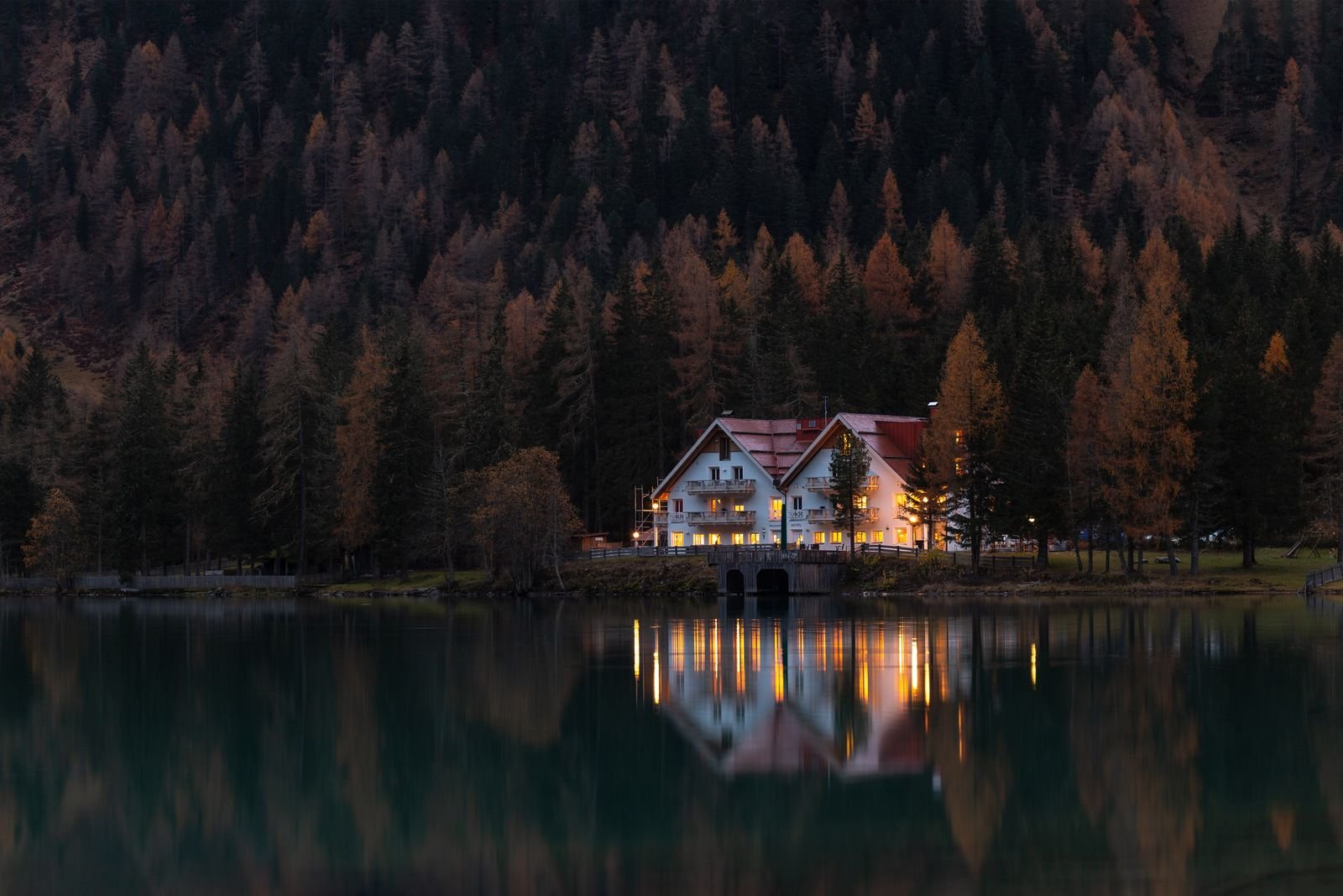 Timber cabin on a lakeshore backed by forest and mountains